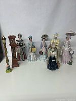 Full group of 6 Mrs Albee Avon figurines plus grandfather clock and floral lamppost, all displayed on a white surface against plain backdrop.