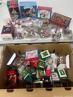 Box displaying a large assortment of miniature Christmas ornaments in various branded boxes and loose pieces in plastic bags.