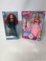 Two boxed Disney Princess dolls side by side; Merida from Brave and Cinderella fantasy fashions.