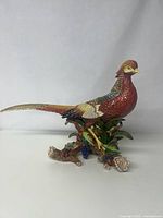 Full view of large glazed ceramic pheasant figurine with long tail and detailed colorful feathers. Sits on base with leaves and berries.