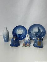 Porcelain item collection including blue and white plates, porcelain bells, bud vase, and miniature robins arranged on flat surface.