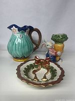 Three vintage Fitz and Floyd ceramic pieces photographed together on white background: green pitcher, bunny vase, and Christmas dish.