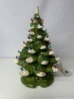 Front view of the 16 inch green ceramic Christmas tree with multicolored bulb lights and white snow accents on branches, with cord attached and plugged in the base.