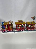 Full view of the three connected ceramic Disney Christmas train pieces on track detail including the engine, two cars, and several Disney characters.