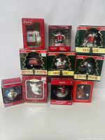 Overview of all nine boxed Coca Cola Christmas ornaments showing variety and condition of boxes and items.