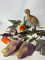 Photo showing assortment of toy dinosaurs and reptiles including large T-Rex figure, smaller dinosaur figures, and purple McDonald's dinosaur hand puppets.