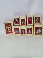 Ten Hallmark Keepsake Christmas ornaments in their boxes, arranged in three rows showing front of boxes with various ornament designs, red and cream box colors.