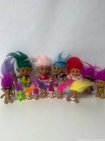 Wide group photo of 15 vintage troll dolls of various sizes and colors, some miniature and some dressed, arranged in rows.