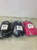 Three pairs of kids mittens size 4/5 in black, navy blue, and bright pink, each in sealed plastic packaging, displayed on a flat surface.