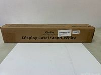 Photo of the unopened brown cardboard box labeled 'Ohuhu Display Easel Stand-White'. The packaging states the product is made in Yiwu, China.