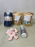 Photo showing Unnivoll blue printed baby crib sheets, two packs of Baja Baby bath bombs and a pink elephant baby rattler, a bottle of Baja Baby shampoo and body wash.