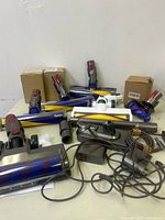 Various Dyson vacuum parts and accessories including multiple vacuum heads and adapters on a white surface.