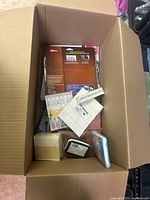 Box with assorted stationery items including packages of glue sticks and other supplies packed at the bottom and sides.