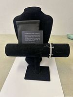 Front view of the Cuban bracelet draped on a black velvet display stand with dust bag and authenticity card behind