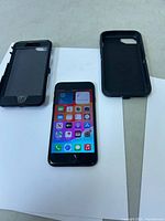 Apple iPhone SE front view powered on with two black protective cases on a white surface