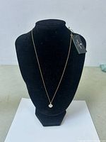 Front view of the gold-tone Kate Spade necklace with floral pendant displayed on a black stand.