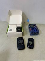 Four phones and devices including Verizon Kyocera flip phone, ZTE flip phone, ZTE device in box, and small keypad device in box