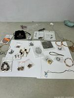 Overview of costume jewelry items laid out on table including earrings, necklaces, bracelets, and rings mostly in packaging or plastic bags.