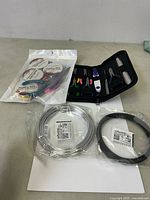 Photo shows two coils of jewelry wire, a black zippered pouch containing jewelry making pliers and cutters, and a sealed bag with additional wire spools and accessories.