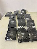 Photo showing 12 pairs of black sheer socks from Rickis, individually packaged on a table.