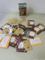 Overview of multiple seed packets spread out on a flat surface with a McKenzie rhubarb seed box standing behind them.
