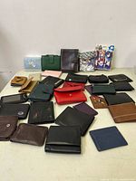 Lot of around 24 wallets displayed on a surface, showing various styles including leather and fabric, many folded bi-fold and tri-fold wallets