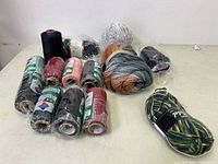 Overview of lot showing multiple skeins of yarn in variegated colors, thread spools, and black waxed polyester cords