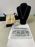 Full display of the Louis Vuitton necklace on black bust stand alongside the dust bag and certificate of authenticity placed on a table.