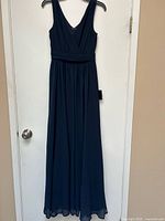 Front view of the navy blue sleeveless evening dress hanging on hanger showing V-neck and waistband.