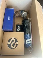 Open cardboard box showing a decorative wooden owl figurine, a blue box with a coiled snake logo, and a Pabst branded item among other objects.