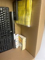 Photo showing keyboard, black cylindrical tube, yellow mailing envelopes, and books in corner of box