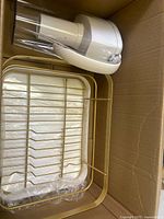 Box containing a white plastic drink dispenser with spout and a gold-colored metal dish drying rack.