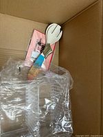 Photo of box interior showing plastic salad serving fork with blue handle, clear plastic container, and packaged items.