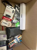 View of box containing USB flash drive, pencils, phone case, and various small packaged items