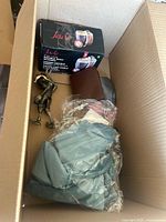 Open box showing brown wallet, decorative figurine, boxed glassware labeled Jade, and folded fabric items in light green and neutral tones.