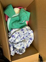 Box showing green knitted sweater and white garment with blue floral/snowflake pattern clothing inside.