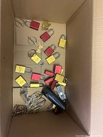 Box with multiple red and yellow padlocks with some keys, metal key rings, and a small black tool or accessory