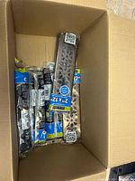 Cardboard box containing multiple sanding belts and small packaged accessories in plastic wrapping with QR codes.