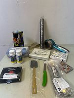 Overview of lot with various new kitchen and household items displayed on table including corkscrew, spatula, knife, cleaning kit, bottles, aluminum foil, napkins, shoe covers