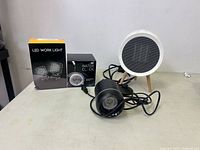 Wide shot showing all four items: LED work light box, water clock box, round mini fan heater, and small light with cable