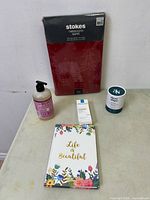 Full lot image showing Stokes Christmas tablecloth in packaging, Life is Beautiful paper book, Mrs. Meyer's lavender hand soap, La Roche-Posay Toleriane Sensitive Creme in box, and Three Ships Dream Night Cream packaged container.
