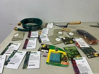 Overview of all items including seed packets spread flat, coiled green garden hose, hand trowel, and plant food spikes