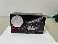 Front view of the black box showing the embossing seal and embossing seal text with silver seal graphic.