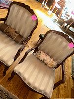 Pair of fabric upholstered sitting chairs with wooden frames and carved detailing, each with a decorative bolster pillow. Chairs placed on hardwood floor.