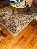 Wool area rug under a wooden table showing floral and vine pattern in beige, green, and burgundy tones.
