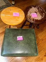 Front view showing two round wooden stools and one square green upholstered ottoman on hardwood floor.