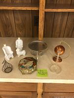 Overview of all items on counter: Avon figurines, octagonal glass box, large candle holder, copper candle holder, bud vase, seashells