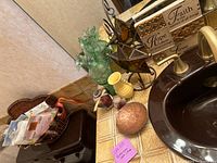 Bathroom countertop with variety of decorative and scent items placed near sink, including basket with papers and trash can underneath counter
