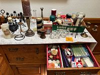 Overview of a large assembly of candles, assorted metal candle holders in various styles, glass candle holders, and a box containing matchbooks and matchboxes displayed on a table.