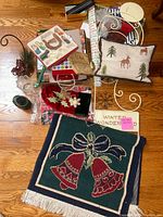 Wide view photo showing various Christmas decor items on wooden floor including pillow, throw rug, stocking, sign, and boxed wrapping paper.